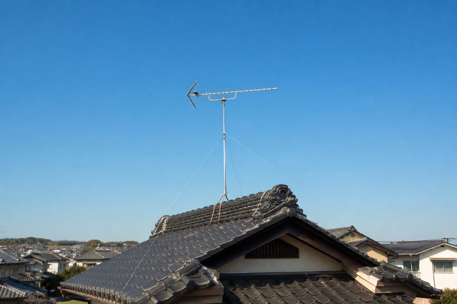 青空の下、瓦屋根に設置されたテレビアンテナのある日本の住宅街